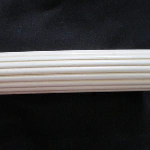 May include: A cylindrical rod with a smooth, off-white finish and a series of parallel, vertical ridges running along its entire length. The object is straight and uniform, featuring a consistent texture of raised lines that create a ribbed appearance.