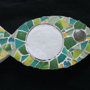 May include: A mosaic fish-shaped picture frame with a white background, green, blue, and yellow tiles, and a clear glass tile in the eye.