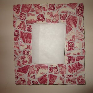 May include: A square picture frame with a white background and a red and white mosaic border. The mosaic is made of small pieces of broken china.