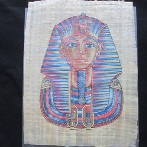 May include: A hand-painted papyrus depicting a pharaoh's mask with blue and red stripes, gold accents, and a detailed face.