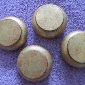 May include: Four antique, round cabinet knobs with a distressed gold finish. The knobs have a circular design with a raised center and are set against a purple textured background.
