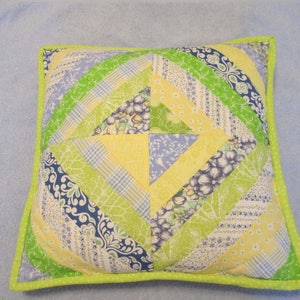 May include: A square pillow with a patchwork design featuring yellow, green, and blue floral fabrics. The pillow has a lime green border.