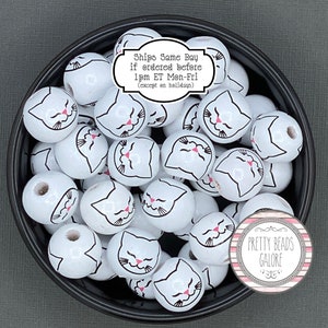 May include: A bowl filled with white wooden beads, each with a black and pink cat face design. The beads are for crafting and jewelry making. The text on the label reads "Ships Same Day if ordered before 1pm ET Mon-Fri (except on holidays)" and "PRETTY BEADS GALORE".