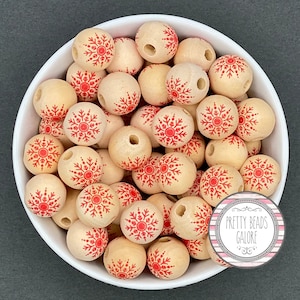 May include: A bowl filled with wooden beads, each bead is decorated with a red snowflake design. The beads are perfect for crafting and making jewelry.