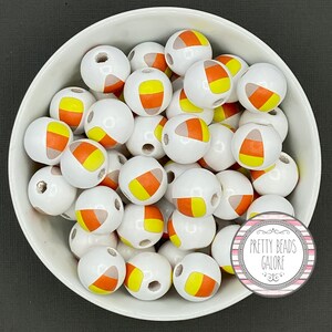 May include: A bowl filled with white wooden beads with a candy corn design. The beads are painted with orange, yellow, and white stripes.