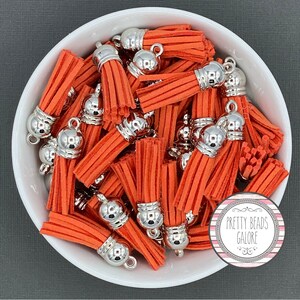May include: A bowl filled with orange suede tassels with silver metal caps and loops. The tassels are approximately 1 inch long.
