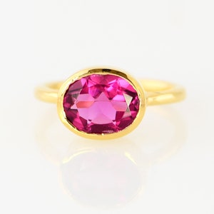 May include: A gold ring with a pink oval gemstone set in a bezel setting.