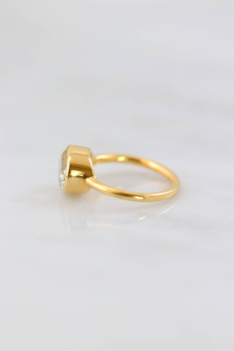 May include: A gold ring with a clear oval-shaped gemstone set in a bezel setting.