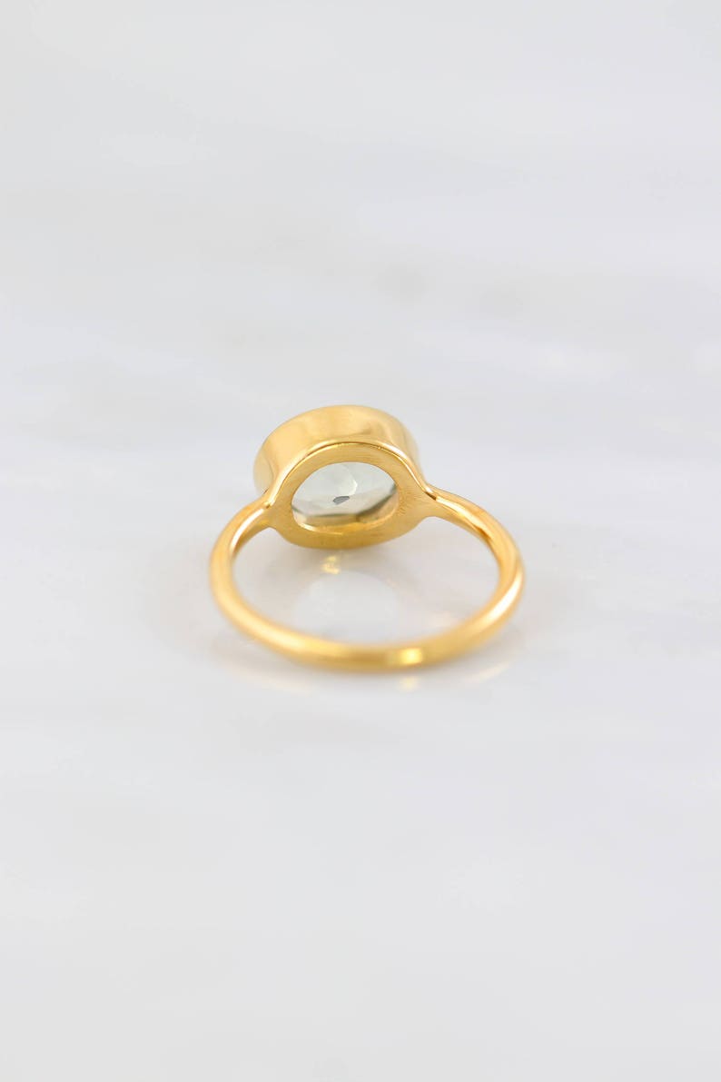 May include: A gold ring with a clear oval-shaped gemstone set in the centre.