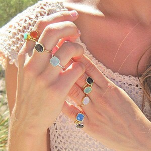 Puede incluir: Un maniqu&iacute; de mano con una variedad de anillos de oro con piedras preciosas de diferentes colores. Los anillos presentan piedras de forma cuadrada en tonos de azul, verde, naranja y negro.