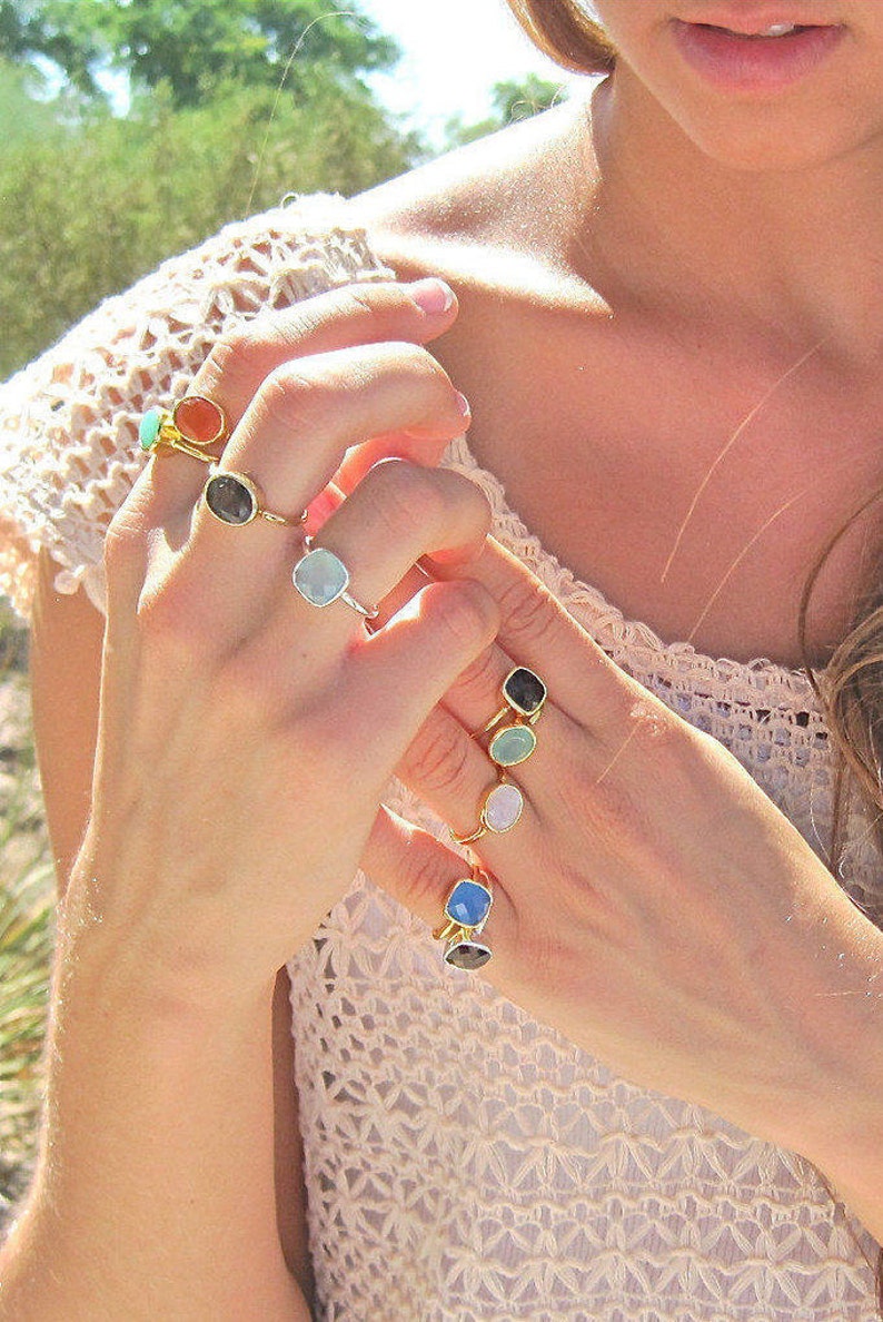 Puede incluir: Un maniqu&iacute; de mano con una variedad de anillos de oro con piedras preciosas de diferentes colores. Los anillos presentan piedras de forma cuadrada en tonos de azul, verde, naranja y negro.