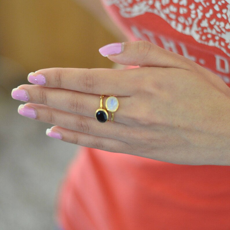 Puede incluir: Dos anillos de oro con piedras preciosas de forma ovalada. Un anillo tiene una piedra blanca y el otro una piedra negra.