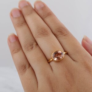 Puede incluir: Un anillo de oro con una piedra ovalada de color rosa claro.