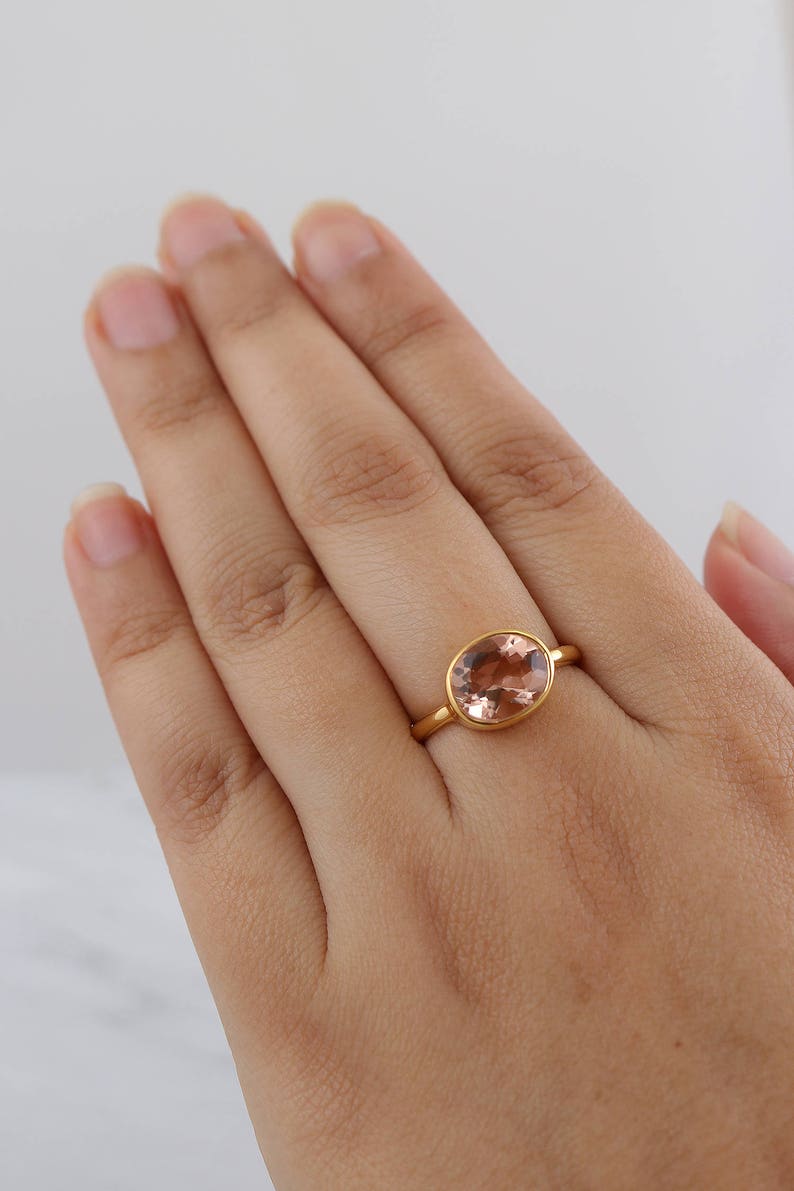 Puede incluir: Un anillo de oro con una piedra ovalada de color rosa claro.