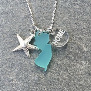 May include: A silver chain necklace with a turquoise blue New Jersey state charm, a silver starfish charm, and a clear round charm with the word "HOME" inscribed on it.