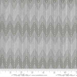 May include: A gray and white herringbone fabric with a subtle sheen. The fabric is shown with a ruler for scale, with the text "moda" printed on the ruler.