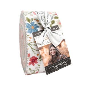 May include: A roll of fabric with a floral pattern featuring blue, red, and pink flowers on a white background. The fabric is tied with a white ribbon and a tag with the "moda FABRICS + SUPPLIES" logo and a woman's portrait.
