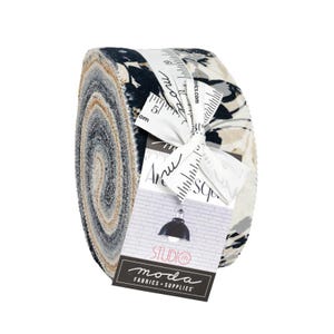 May include: Rolled fabric bundle with a variety of patterned fabrics in shades of blue, beige, and gray. The bundle is tied with a white ribbon and includes a tag with the "Studio Moda Fabrics + Supplies" logo.