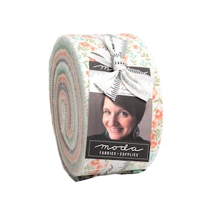 May include: A roll of fabric featuring a floral print in shades of pink, green, and white. The fabric is rolled up and tied with a white ribbon. The label on the fabric reads "Moda Fabrics + Supplies".