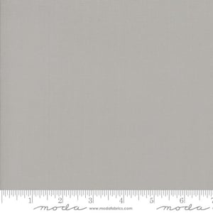 May include: A solid gray fabric swatch with a subtle texture. The fabric is measured in inches with a ruler at the bottom of the image. The ruler has the word "moda" printed on it.