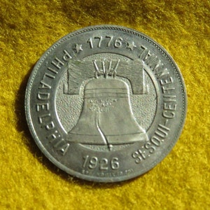 May include: Silver coin with the inscription "Philadelphia 1776 - 1926 Sesqui-Centennial" and a depiction of the Liberty Bell.
