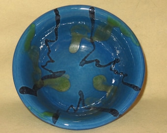 May include: A blue ceramic bowl with black and green abstract designs. The bowl is glazed and has a glossy finish.