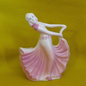 May include: A white ceramic figurine of a woman in a pink dress. The woman is dancing and her dress is flowing behind her. The figurine is a vintage planter.