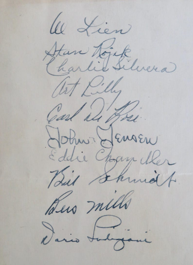 May include: A white sheet of paper with a list of names written in blue ink. The names include: W Lien, Atan Dojek, Charlie Silvera, Art Lilly, Carl Dihei, John Jensen, Eddie Cham, Bil Shund, Bus mills, and Dario Fabjani.