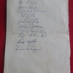 May include: A white piece of paper with a list of names written in blue ink. The names include: Lien, Atan Dojek, Charlie Silvera, Art Lilly, Carli, John Jensen, Eddie Chayther, Bit Shund, Bus Mills, and Dario Fubiani.