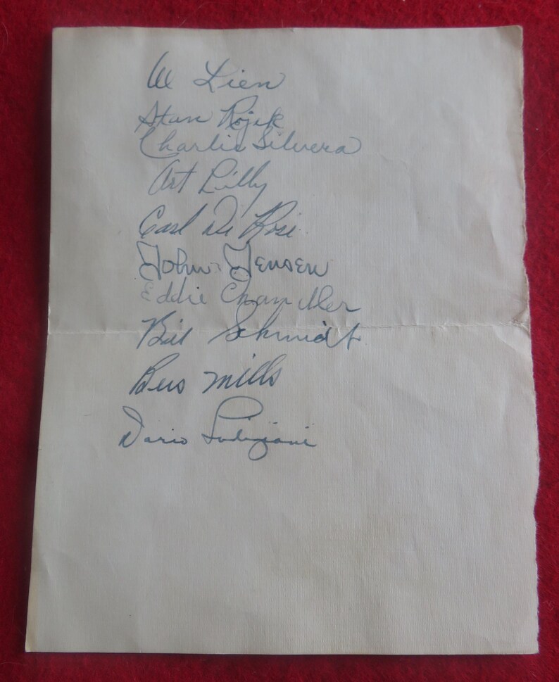 May include: A white piece of paper with a list of names written in blue ink. The names include: Lien, Atan Dojek, Charlie Silvera, Art Lilly, Carli, John Jensen, Eddie Chayther, Bit Shund, Bus Mills, and Dario Fubiani.