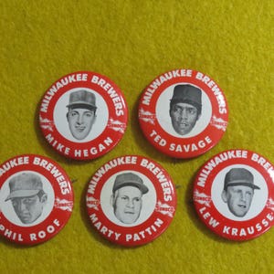May include: Five vintage Milwaukee Brewers baseball team pinback buttons. Each button is red with white text and a portrait of a player. The players' names are Mike Hegan, Ted Savage, Phil Roof, Marty Pattin, and Lew Krausse.