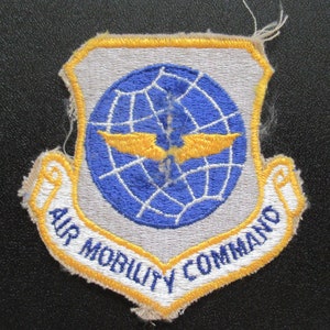 May include: A vintage embroidered patch with a blue globe and yellow wings, surrounded by a white banner with the text "AIR MOBILITY COMMAND".