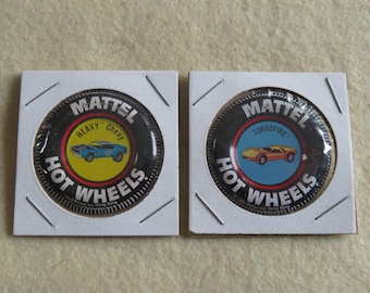 May include: Two black and red Hot Wheels pinback buttons. The left button features a blue car with the text "Heavy Chevy" and the right button features an orange car with the text "Turbofire".