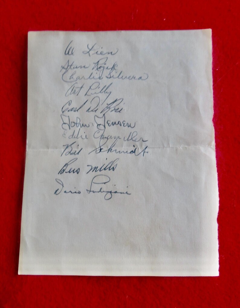 May include: A white piece of paper with a list of names written in blue ink. The names include: Lien, Stun Nojek, Charlie Silvera, Art Lilly, Carl du Hei, John Jensen, Edilie Chogany ther, Paul Schmidt, Bus Mills, and Dario Fubigani.