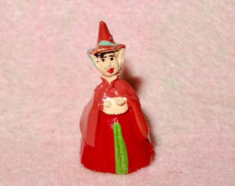 Puede incluir: Una pequeña figurita pintada de rojo y verde de un hada que lleva un sombrero puntiagudo con un diseño azul y blanco. El hada tiene una cara pintada con una sonrisa y ojos grandes.