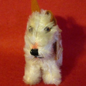 May include: A white plush toy dog with brown ears and black eyes. The dog is standing on a red surface.