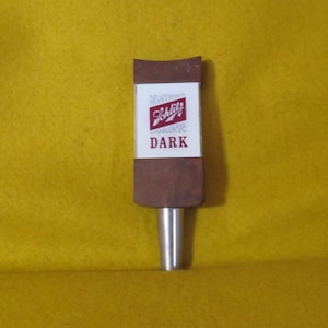 May include: A brown wooden beer tap handle with a white label that says "Schlitz DARK" in red lettering.