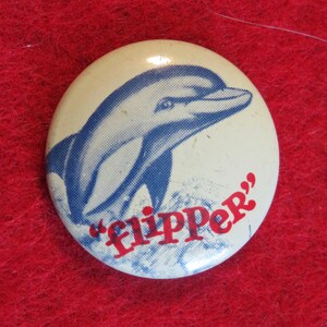 May include: A white button with a blue and white image of a dolphin and the text "Flipper" in red.