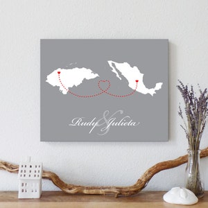 May include: A gray canvas print with a map of Mexico and Honduras. A red dotted line connects the two countries with a heart in the middle. The text "Rudy & Julieta" is written in cursive at the bottom of the print.