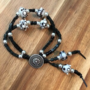 May include: A black and silver bracelet with white and black glass beads. The bracelet has a silver clasp with a floral design.