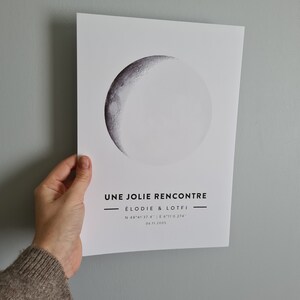 May include: A black and white print with a crescent moon graphic. The text "UNE JOLIE RENCONTRE &Eacute;LODIE & LOTFI N 48&deg;41'37.4" E 6&deg;11'0.274" 06.11.2005" is printed below the moon.