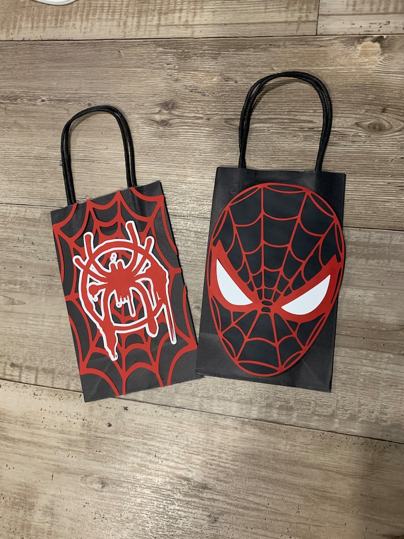 May include: Two black paper gift bags with red and white spider-man designs. One bag has a spider web with a spider in the center. The other bag has a spider-man mask.