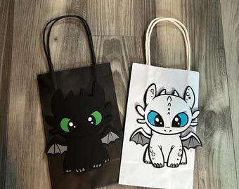 May include: Two paper gift bags with dragon designs. One bag is black with a black dragon with green eyes. The other bag is white with a white dragon with blue eyes. Both bags have handles.