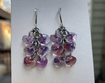 May include: A pair of silver dangle earrings with multiple purple and pink glass beads. The beads are translucent and have a marbled effect.