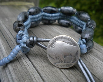 Può includere: Un braccialetto con perline blu e grigie con un ciondolo in nichel da cinque centesimi con un bufalo d'argento. Il braccialetto è realizzato con un cordoncino in pelle e ha un design intrecciato.