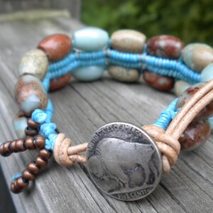 May include: A turquoise and brown beaded bracelet with a leather strap and a silver coin with the text "FIVE CENTS" on it.