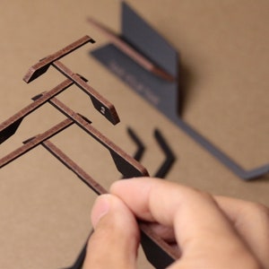 Puede incluir: Un soporte de madera marrón con varios niveles, diseñado para sostener objetos como teléfonos o tabletas. El soporte está hecho de varias piezas que se conectan entre sí.