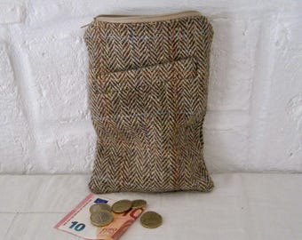 May include: A rectangular pouch made of brown, tan, and grey tweed fabric with a herringbone pattern and a top zip closure. The pouch is positioned above a ten euro banknote and several gold-coloured coins resting on a white surface.