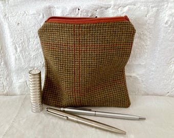 May include: A brown and tan tweed zippered pouch with red accents. The pouch is sitting on a white surface with two silver pens next to it.