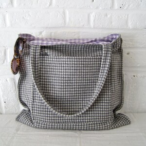 Op de afbeelding: Een grijze en witte geruite tote bag met een paarse en witte geruite voering. De tas heeft twee hengsels en een zakje aan de voorkant.
